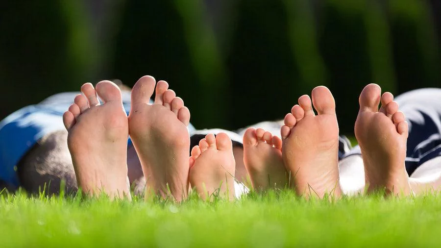 Soles of multiple bare feet belonging to adults and a child lying on grass