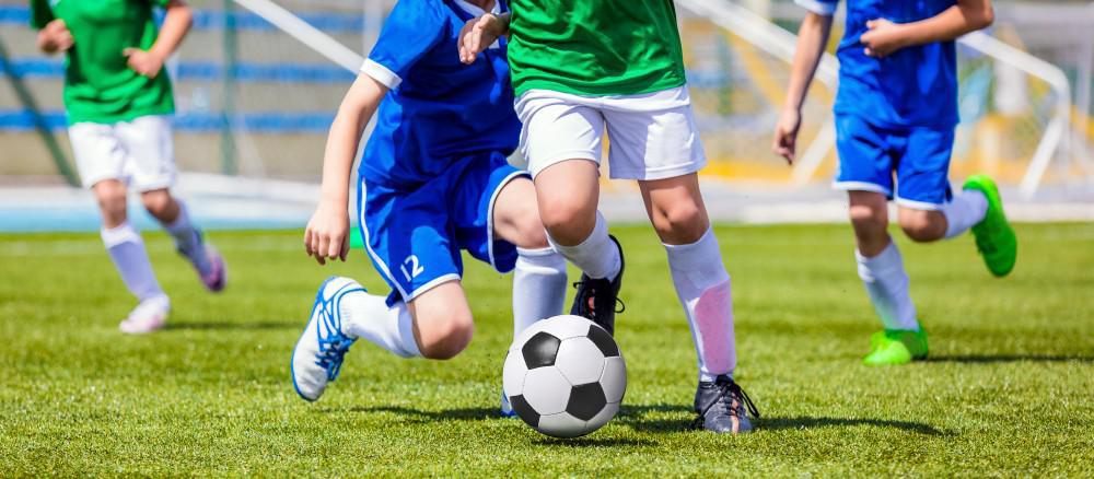 Children wearing soccer cleats running and kicking a football on grass