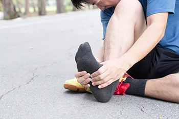 Person sitting on ground gripping the arch of their foot in pain