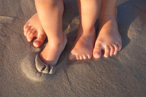 Child's bare feet and adult bare feet standing on sand