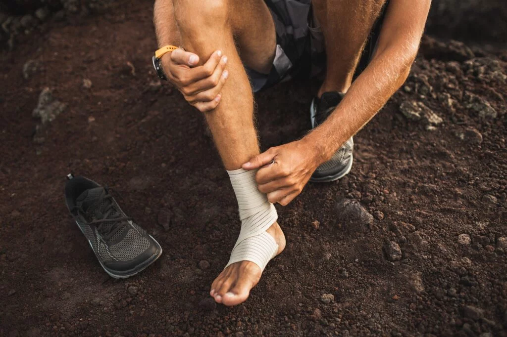 Runner holding a bandaged ankle while sitting outdoors.