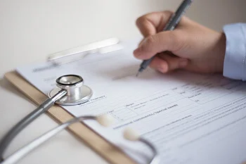 Clinician writing on a medical form beside a stethoscope on a clipboard